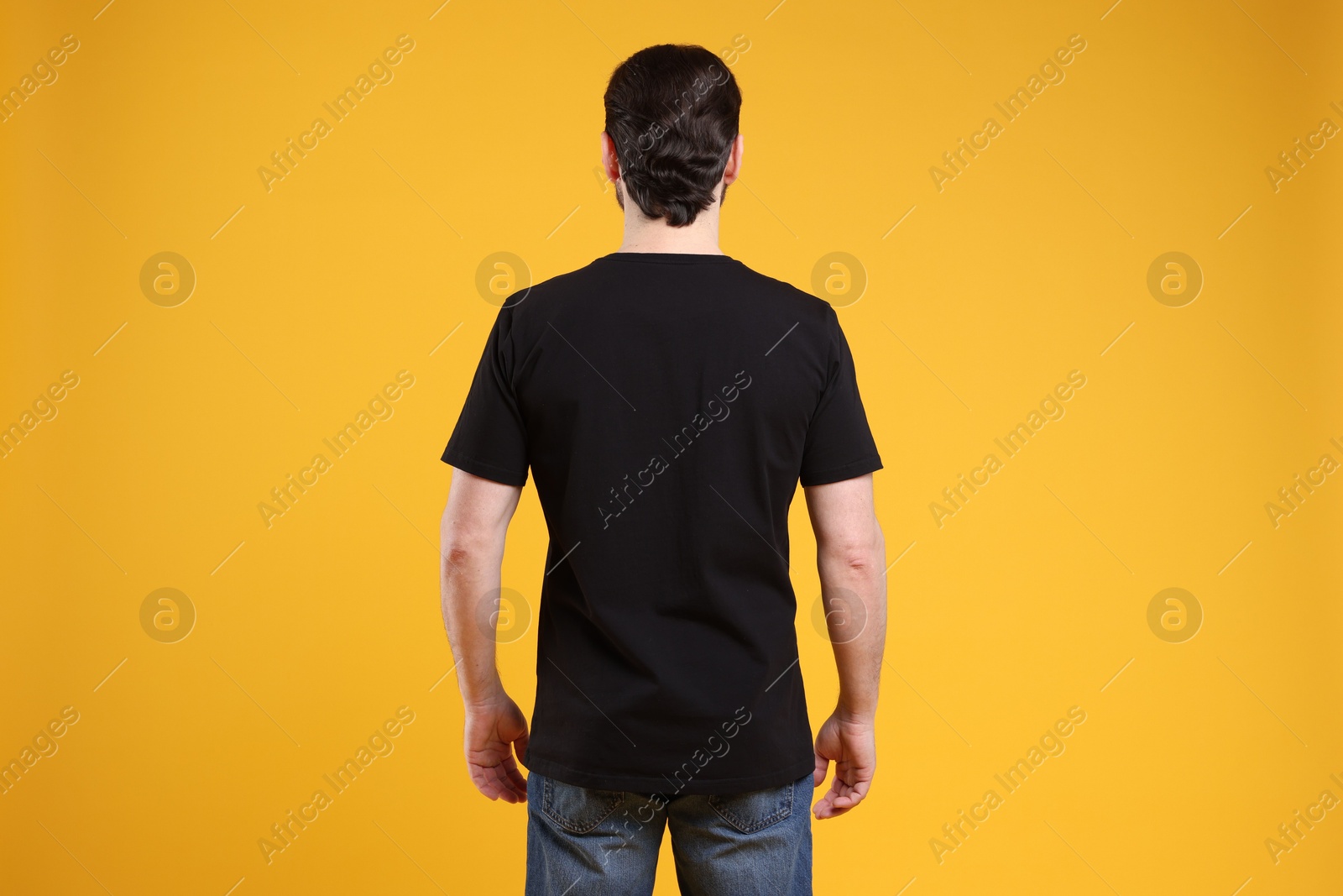 Photo of Man wearing blank black t-shirt on orange background, back view. Mockup for design