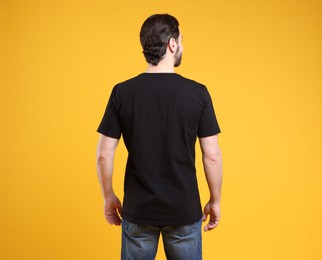 Photo of Man wearing blank black t-shirt on orange background, back view. Mockup for design