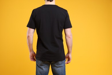 Photo of Man wearing blank black t-shirt on orange background, back view. Mockup for design