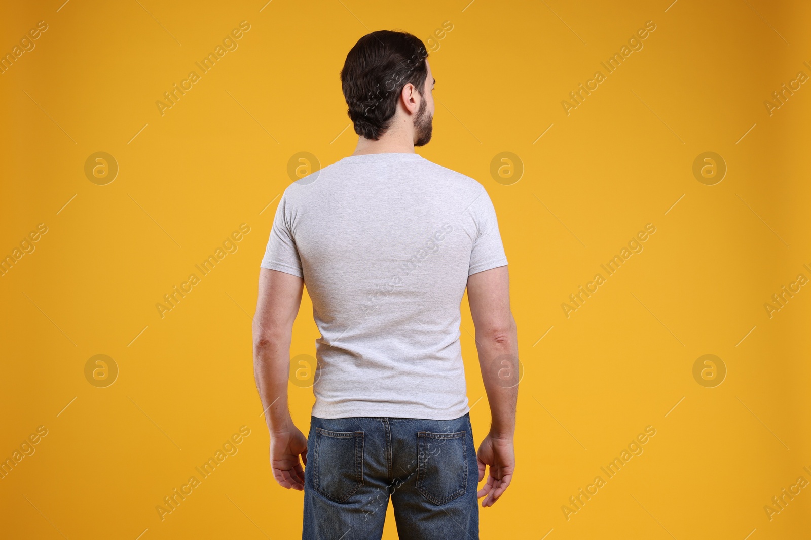 Photo of Man wearing blank white t-shirt on orange background, back view. Mockup for design