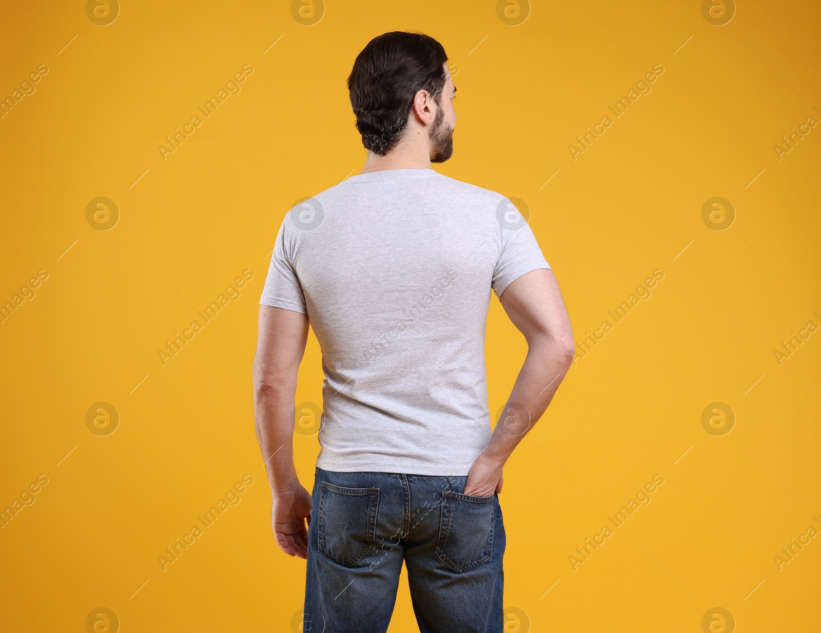 Photo of Man wearing blank white t-shirt on orange background, back view. Mockup for design