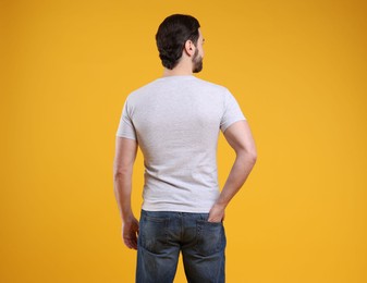 Photo of Man wearing blank white t-shirt on orange background, back view. Mockup for design