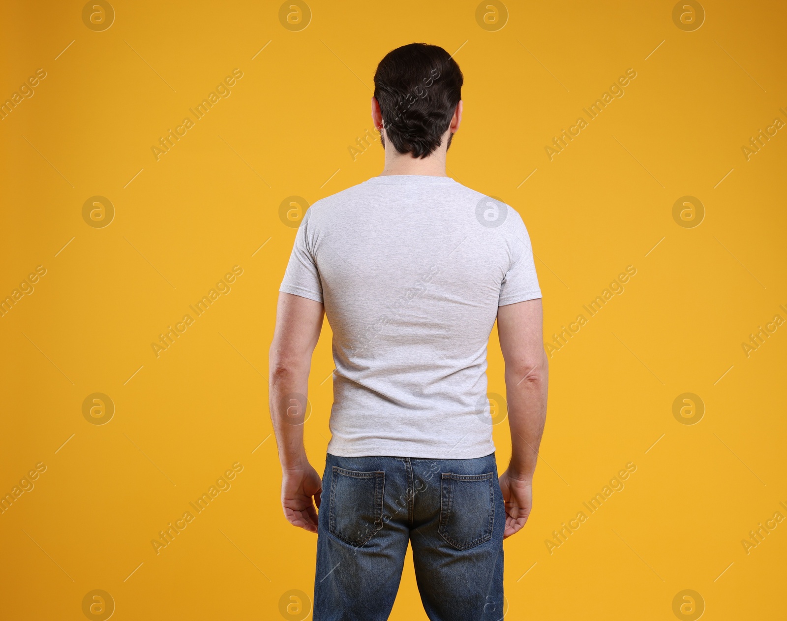 Photo of Man wearing blank white t-shirt on orange background, back view. Mockup for design