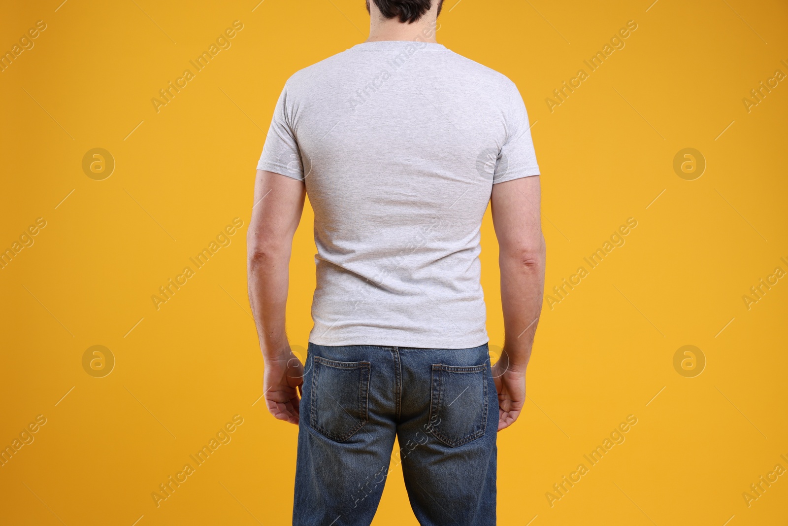 Photo of Man wearing blank white t-shirt on orange background, back view. Mockup for design