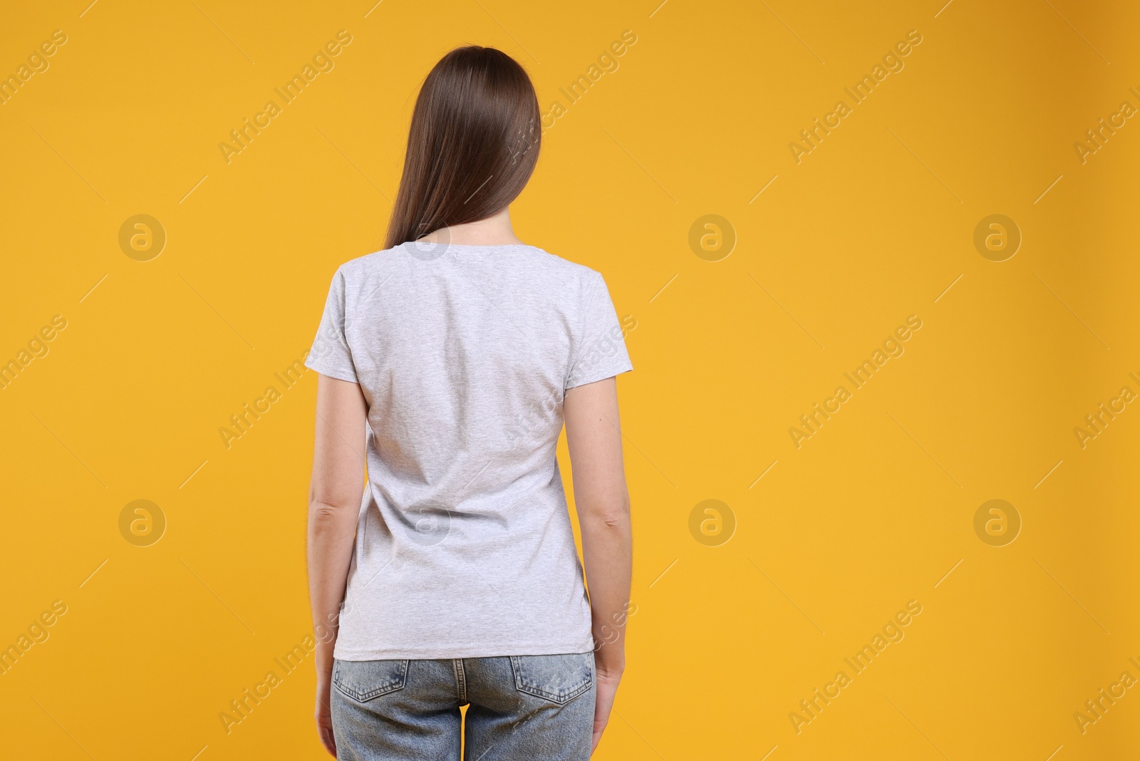 Photo of Woman wearing blank white t-shirt on orange background, back view. Mockup for design