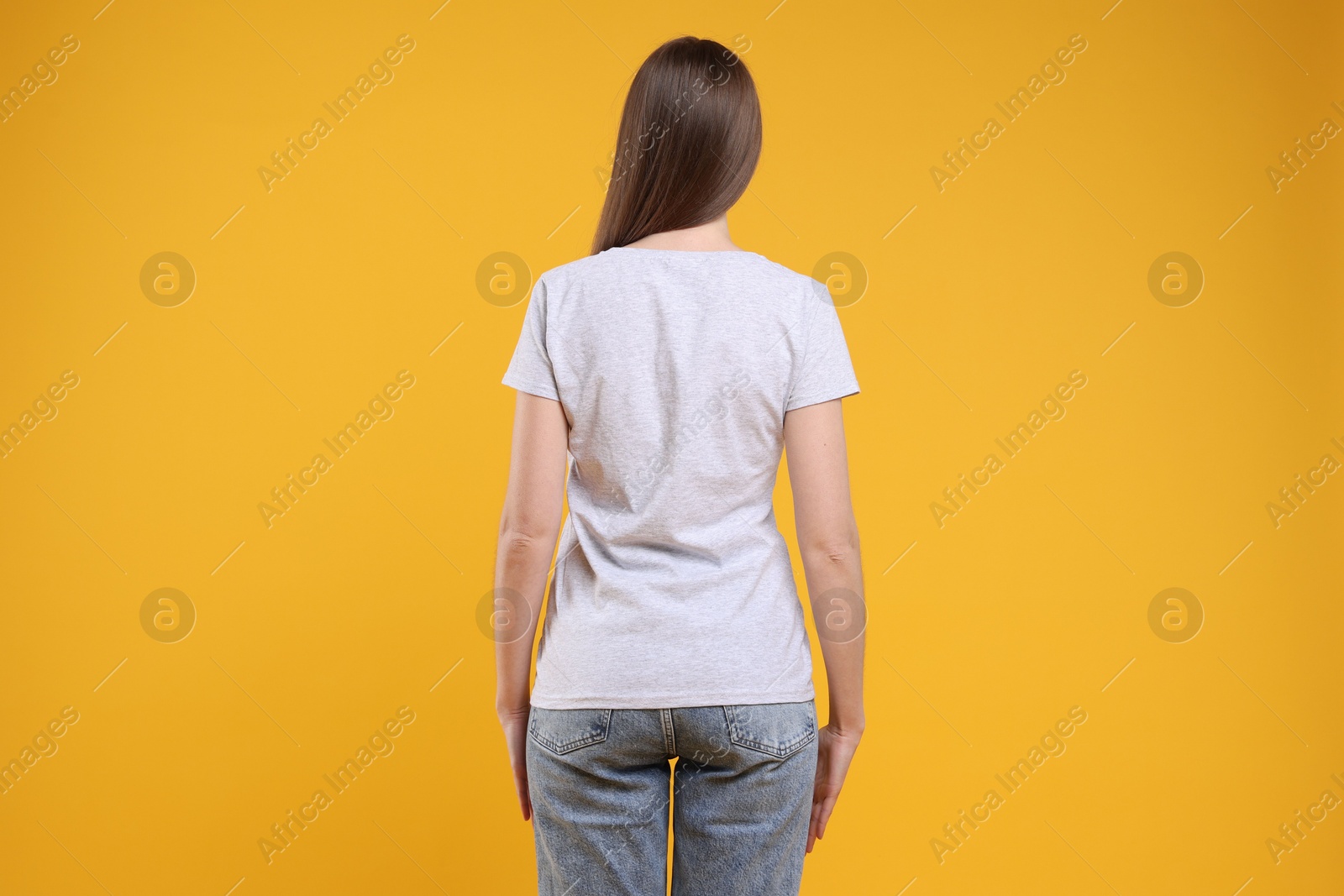 Photo of Woman wearing blank white t-shirt on orange background, back view. Mockup for design