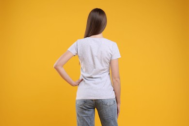 Photo of Woman wearing blank white t-shirt on orange background, back view. Mockup for design