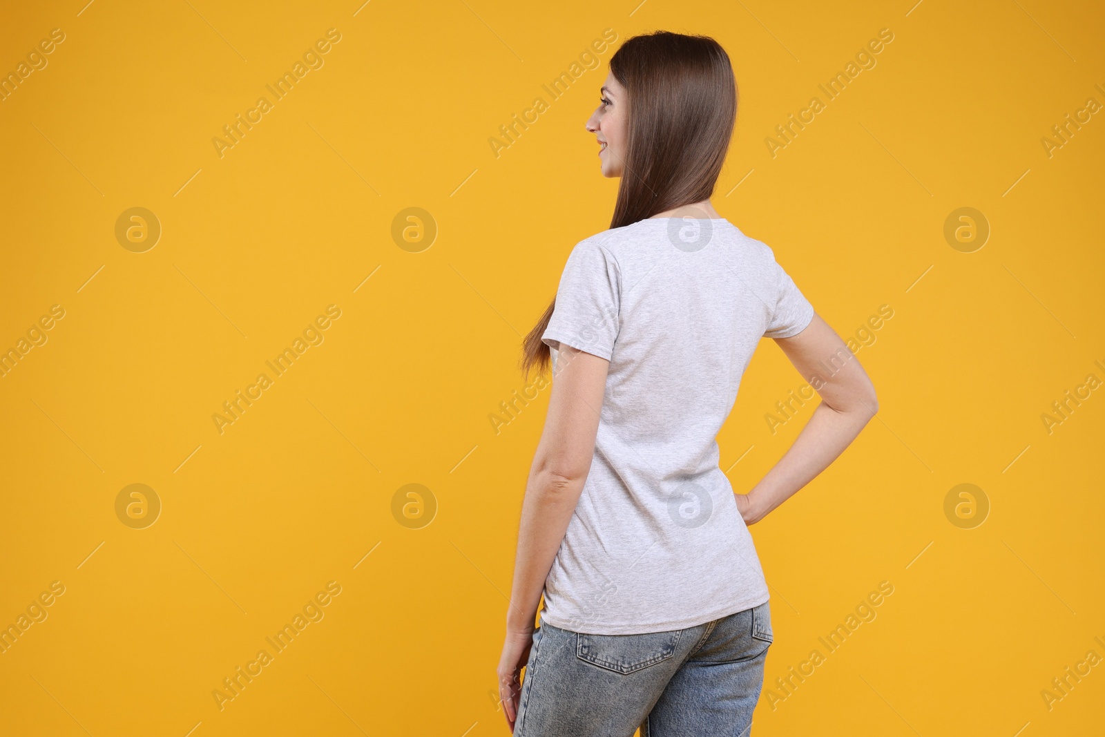 Photo of Woman wearing blank white t-shirt on orange background, back view. Mockup for design