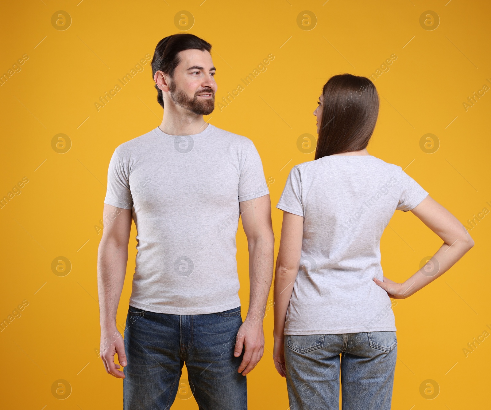 Photo of Woman and man wearing blank white t-shirts on orange background. Mockup for design