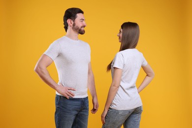 Photo of Woman and man wearing blank white t-shirts on orange background. Mockup for design