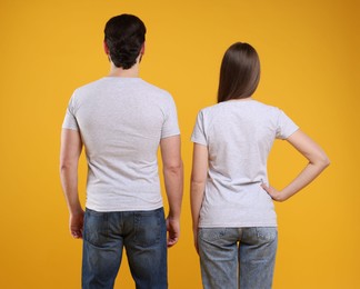 Photo of Woman and man wearing blank white t-shirts on orange background, back view. Mockup for design