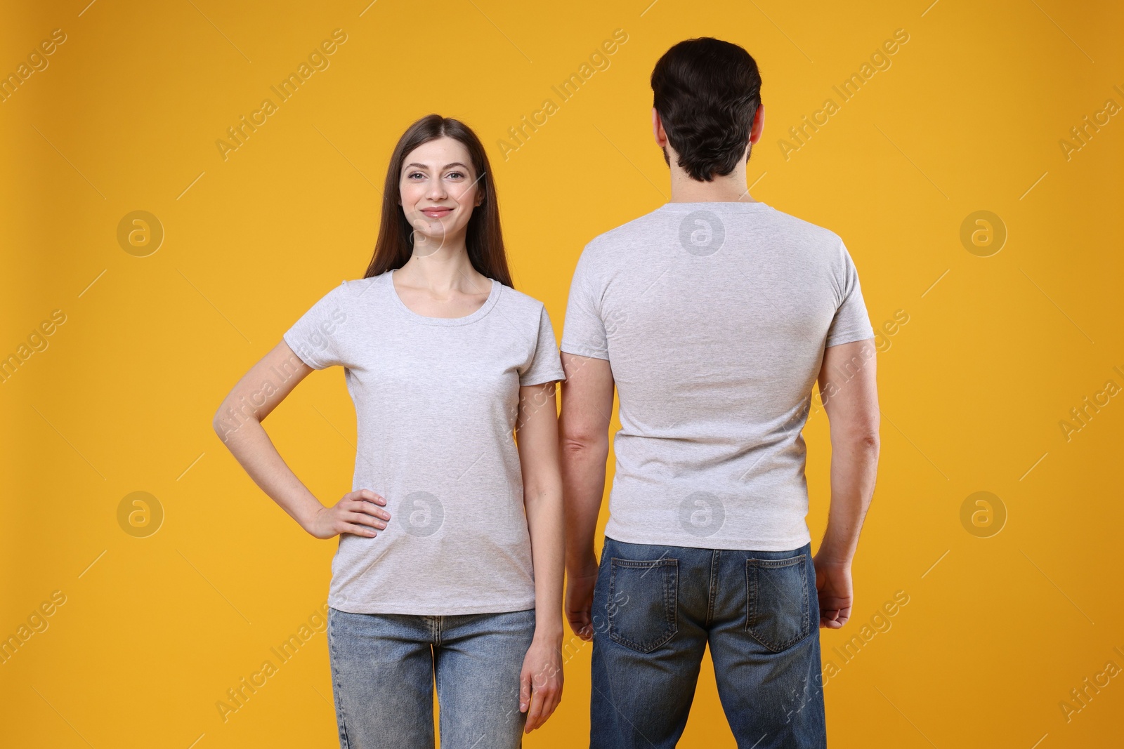 Photo of Woman and man wearing blank white t-shirts on orange background. Mockup for design