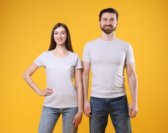 Photo of Woman and man wearing blank white t-shirts on orange background. Mockup for design