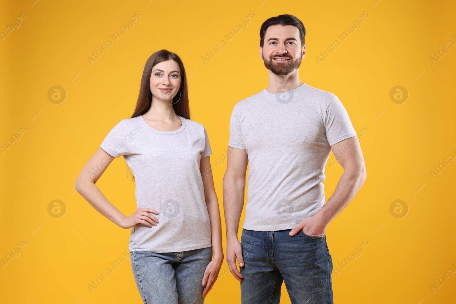 Photo of Woman and man wearing blank white t-shirts on orange background. Mockup for design