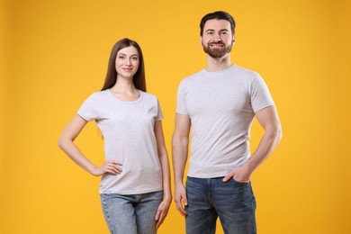 Photo of Woman and man wearing blank white t-shirts on orange background. Mockup for design