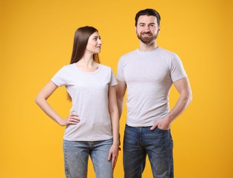 Photo of Woman and man wearing blank white t-shirts on orange background. Mockup for design