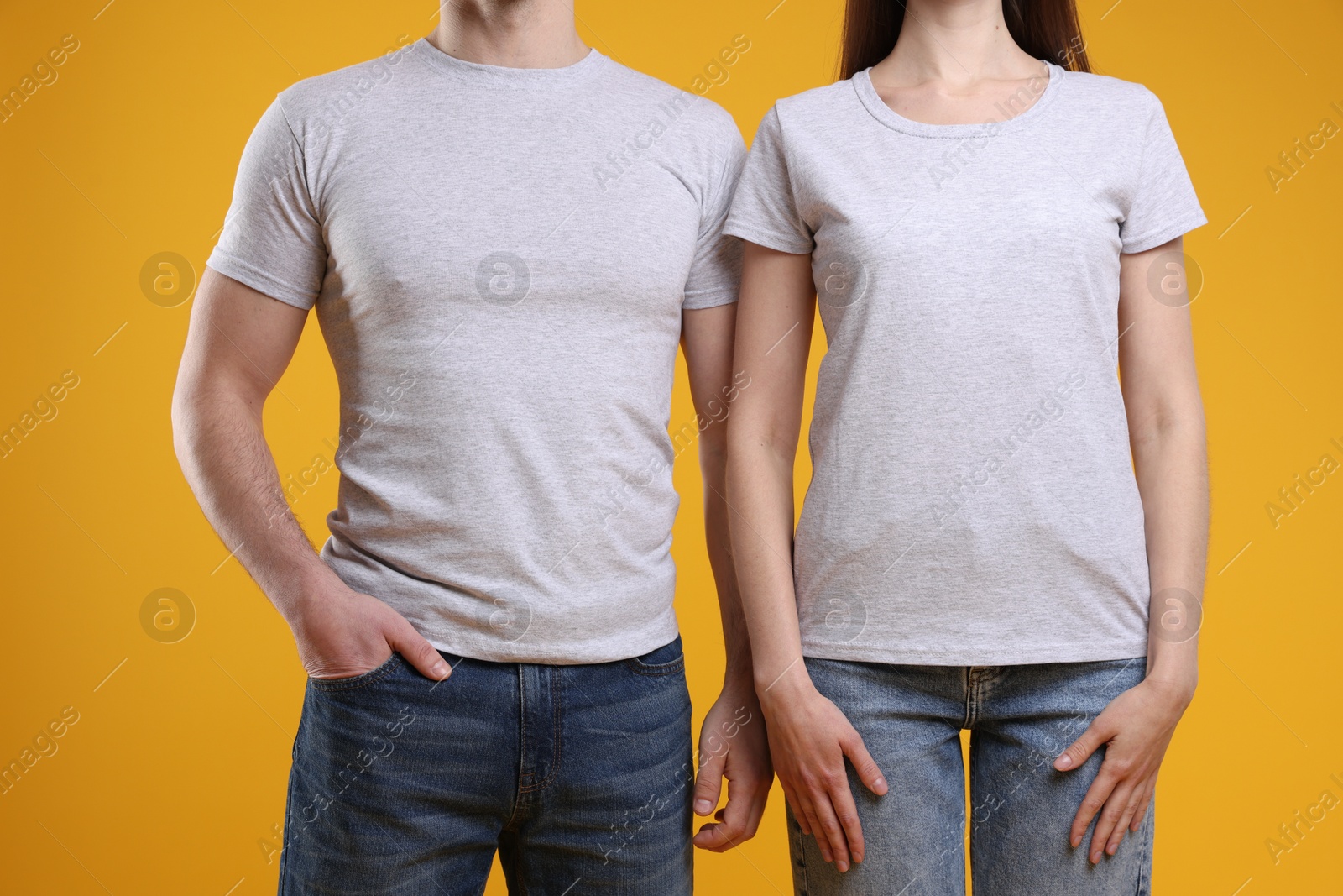 Photo of Woman and man wearing blank white t-shirts on orange background, closeup. Mockup for design