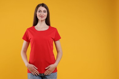 Photo of Woman wearing blank red t-shirt on orange background. Mockup for design