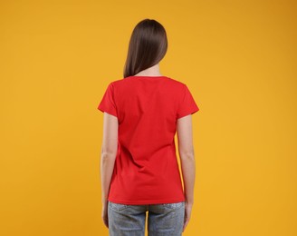 Photo of Woman wearing blank red t-shirt on orange background, back view. Mockup for design