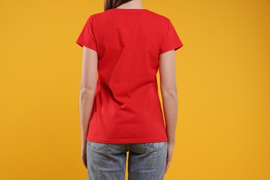 Photo of Woman wearing blank red t-shirt on orange background, back view. Mockup for design