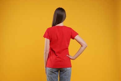 Photo of Woman wearing blank red t-shirt on orange background, back view. Mockup for design