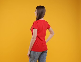 Photo of Woman wearing blank red t-shirt on orange background, back view. Mockup for design