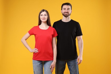 Photo of Woman and man wearing blank t-shirts on orange background. Mockup for design