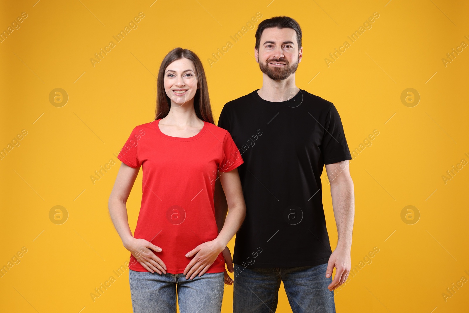 Photo of Woman and man wearing blank t-shirts on orange background. Mockup for design