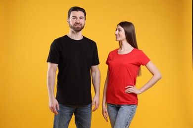 Photo of Woman and man wearing blank t-shirts on orange background. Mockup for design