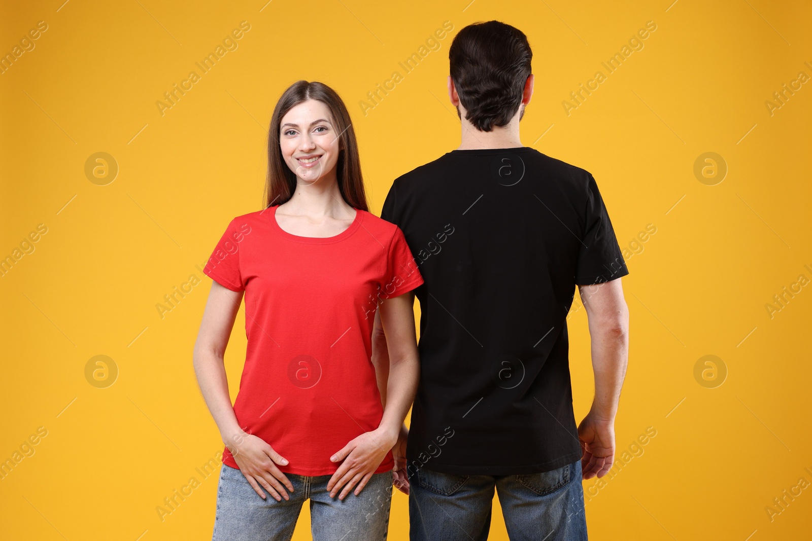 Photo of Woman and man wearing blank t-shirts on orange background. Mockup for design