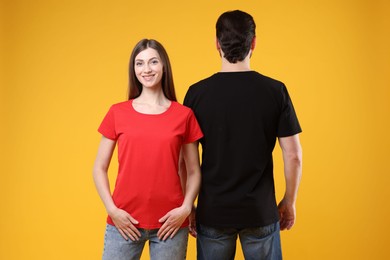 Photo of Woman and man wearing blank t-shirts on orange background. Mockup for design