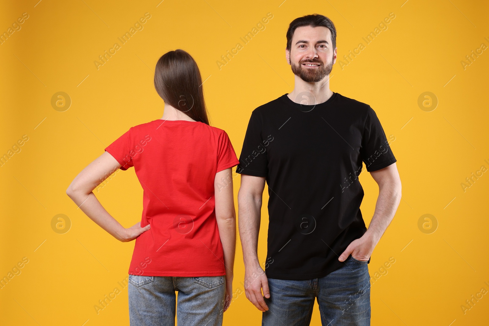 Photo of Woman and man wearing blank t-shirts on orange background. Mockup for design