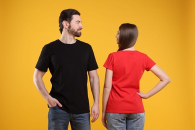 Photo of Woman and man wearing blank t-shirts on orange background. Mockup for design