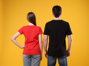 Photo of Woman and man wearing blank t-shirts on orange background, back view. Mockup for design