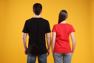 Photo of Woman and man wearing blank t-shirts on orange background, back view. Mockup for design