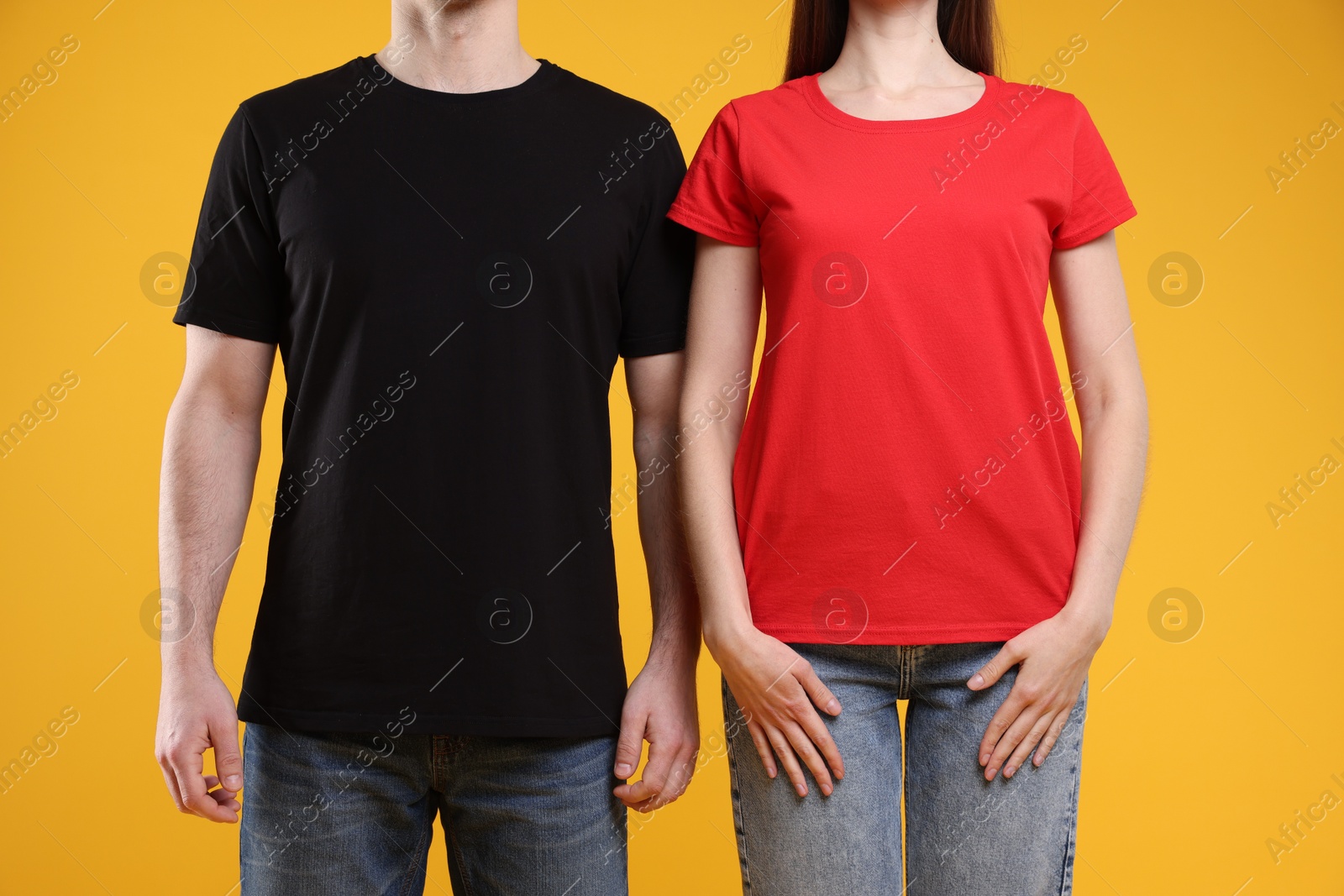 Photo of Woman and man wearing blank t-shirts on orange background, closeup. Mockup for design