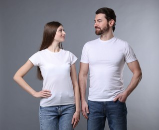 Photo of Woman and man wearing blank white t-shirts on light grey background. Mockup for design