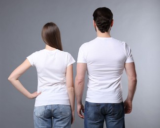 Photo of Woman and man wearing blank white t-shirts on light grey background, back view. Mockup for design