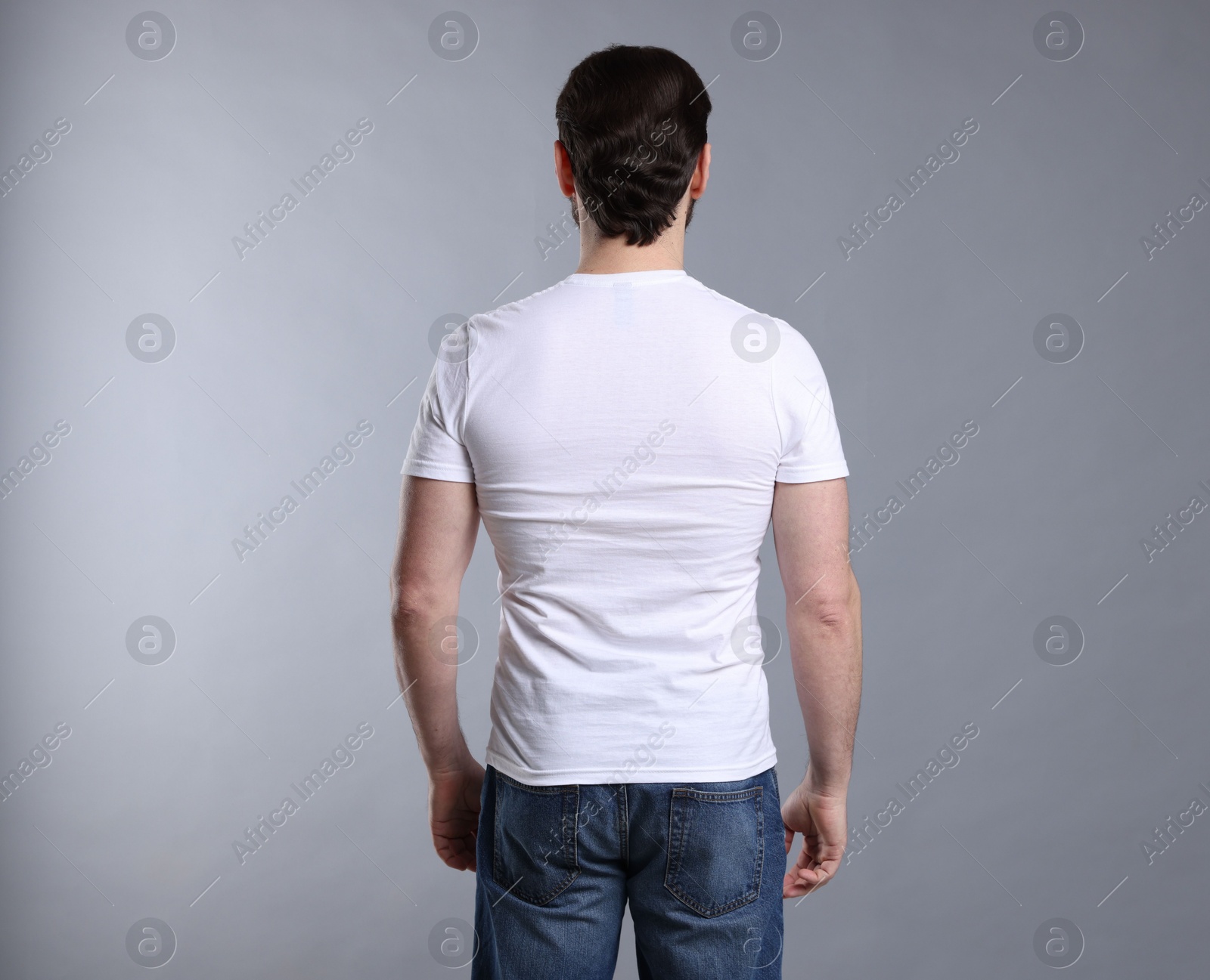 Photo of Man wearing blank white t-shirt on light grey background, back view. Mockup for design