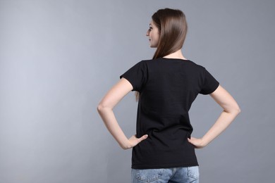 Photo of Woman wearing blank black t-shirt on light grey background, back view. Mockup for design