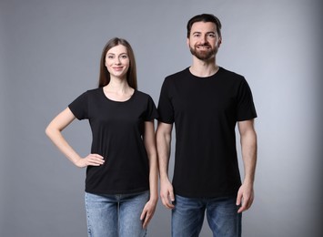 Photo of Woman and man wearing blank black t-shirts on light grey background. Mockup for design