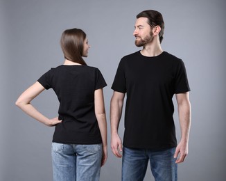 Photo of Woman and man wearing blank black t-shirts on light grey background. Mockup for design