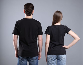 Photo of Woman and man wearing blank black t-shirts on light grey background, back view. Mockup for design