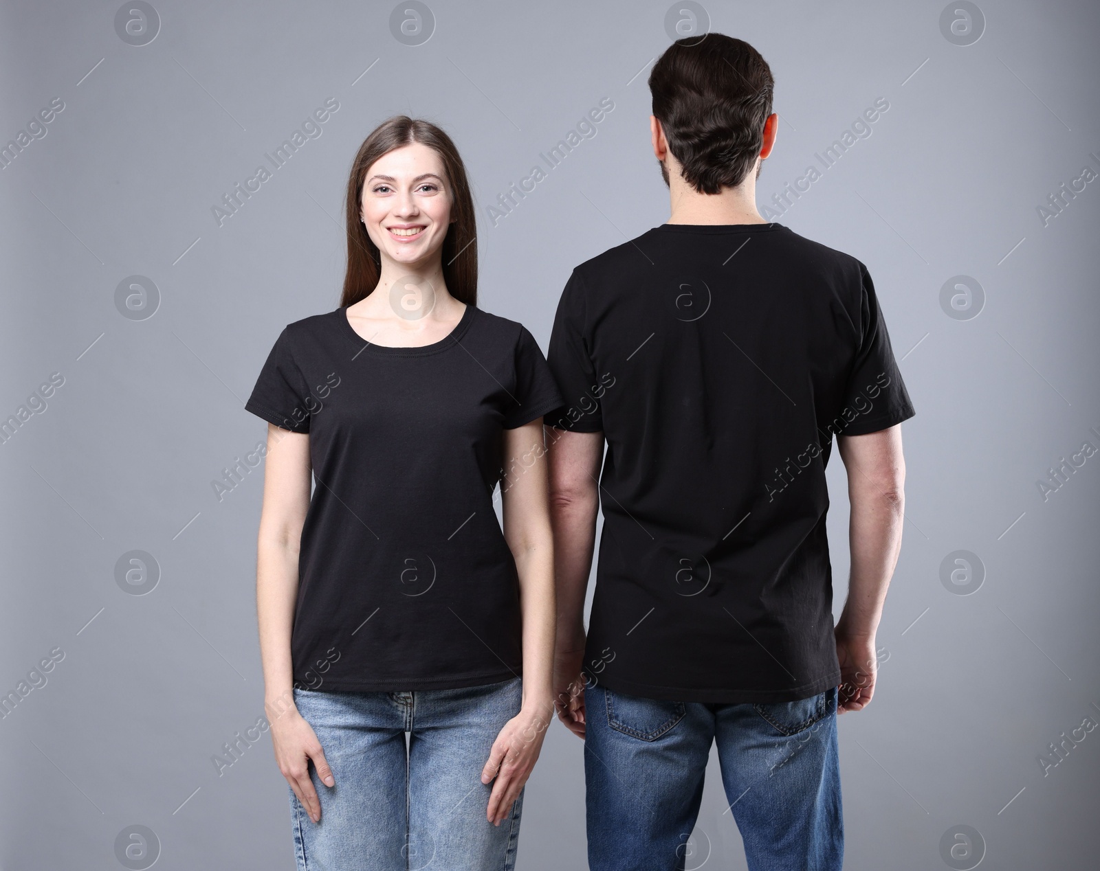 Photo of Woman and man wearing blank black t-shirts on light grey background. Mockup for design