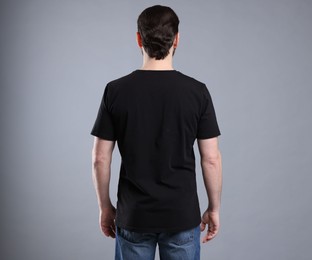 Photo of Man wearing blank black t-shirt on light grey background, back view. Mockup for design