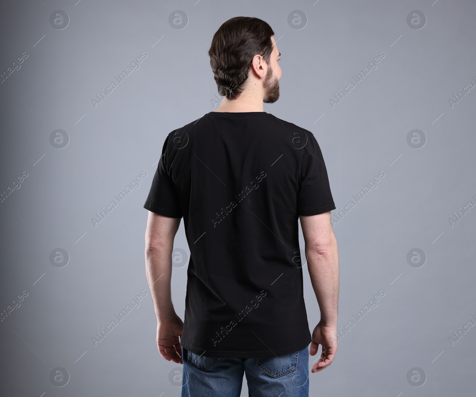 Photo of Man wearing blank black t-shirt on light grey background, back view. Mockup for design