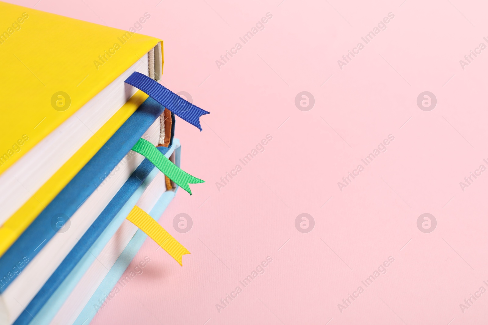 Photo of Books with ribbon bookmarks on pink background, closeup. Space for text