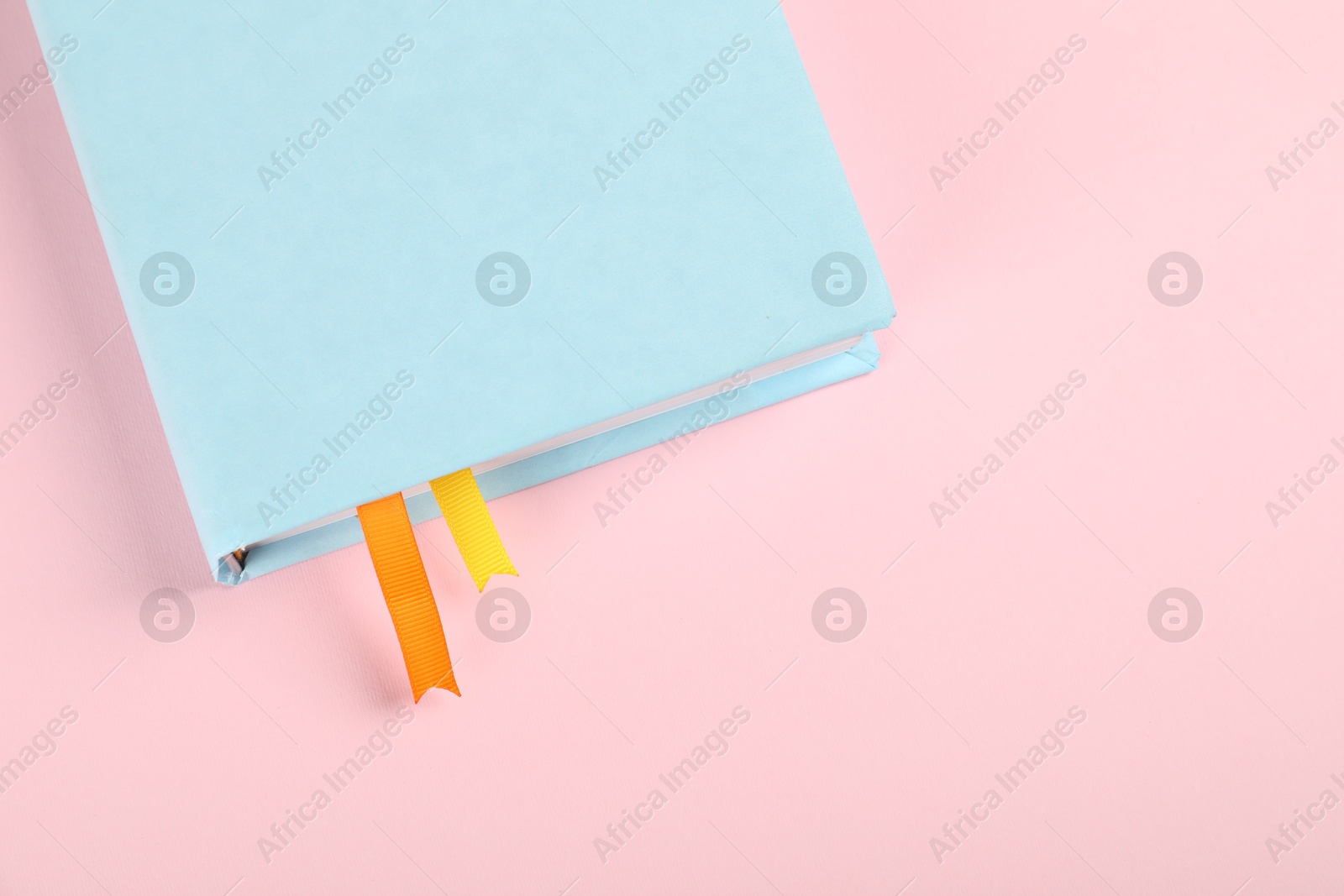 Photo of Book with ribbon bookmarks on pink background, above view. Space for text