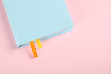 Photo of Book with ribbon bookmarks on pink background, above view. Space for text