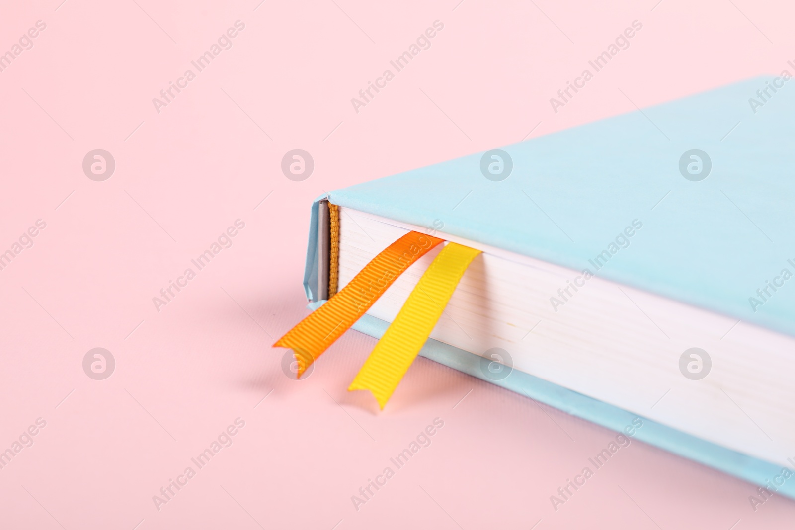 Photo of Book with ribbon bookmarks on pink background, closeup. Space for text